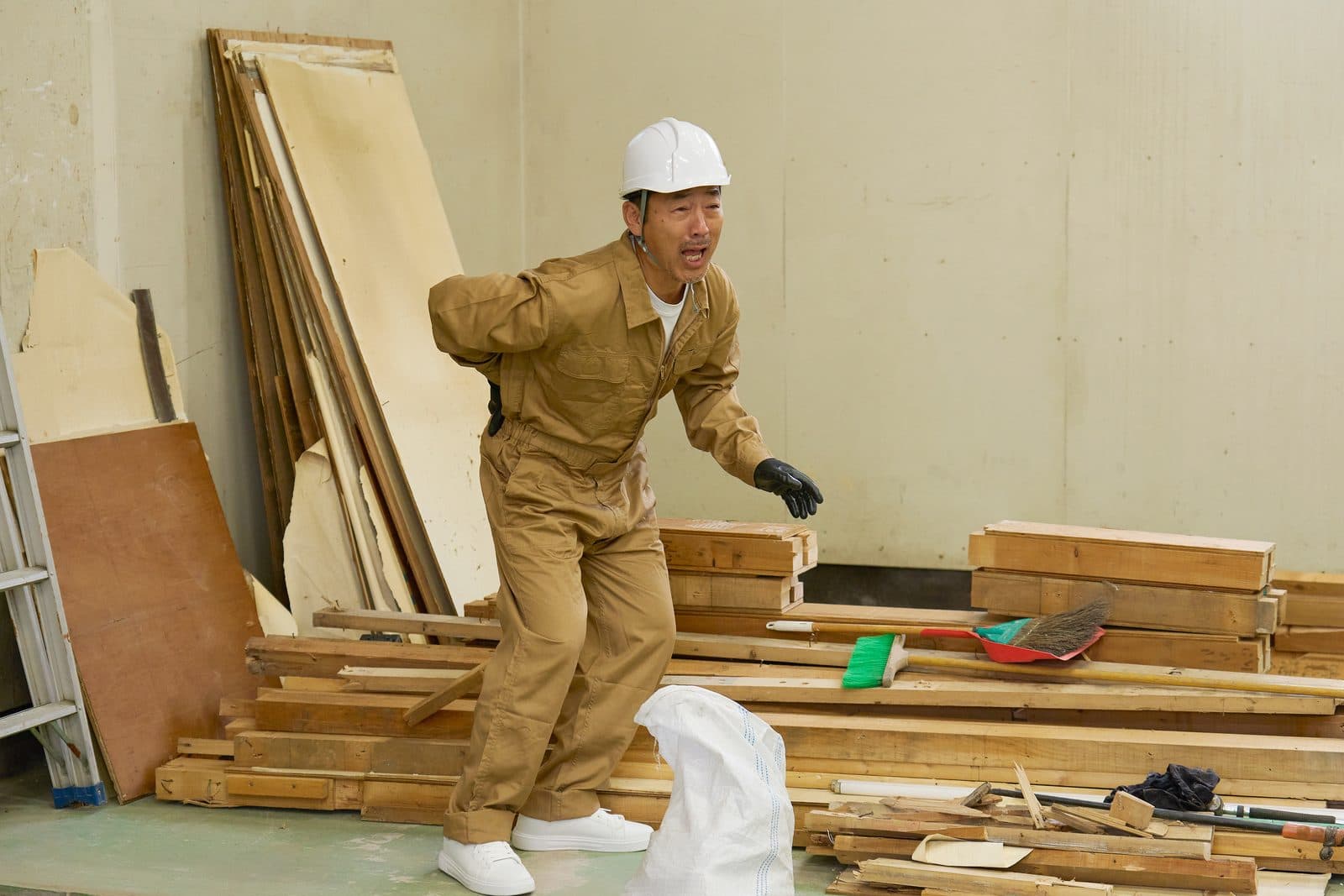 解体現場で資材を持ち上げかけ、腰を押さえる職人