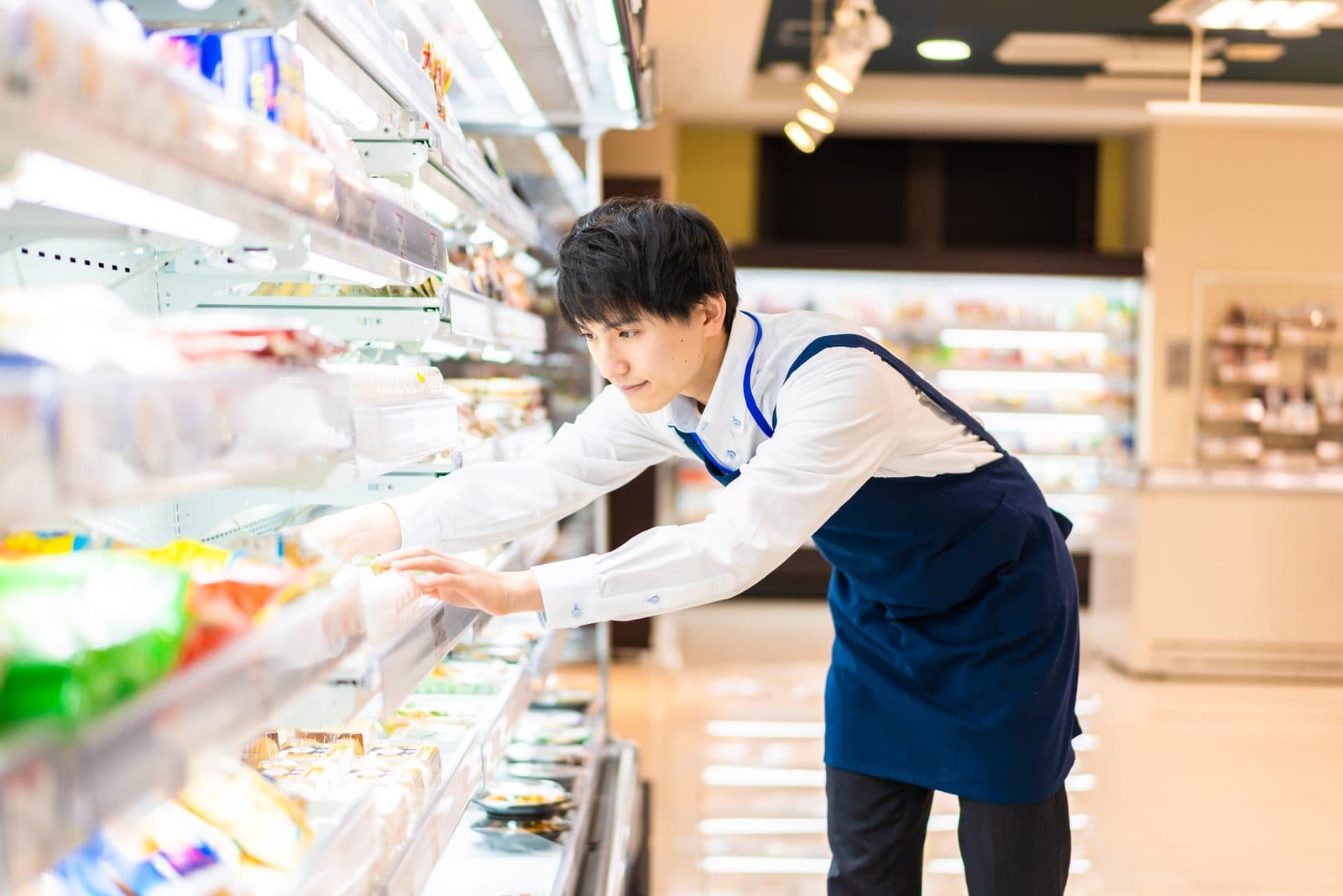 食品スーパーの売場で、棚に商品を並べる店舗スタッフ